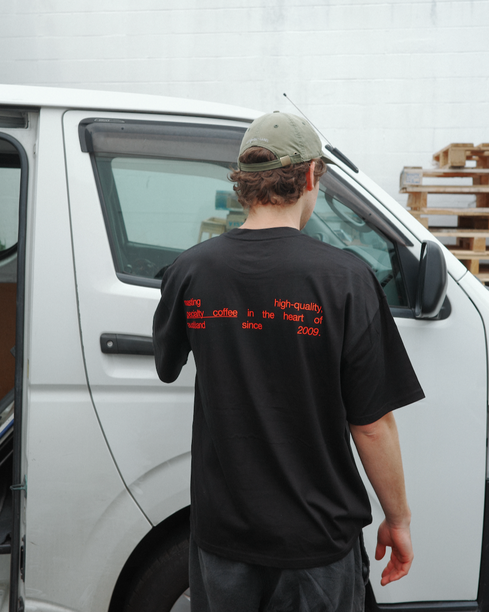 Person wearing a black t-shirt with red text standing next to a white van.